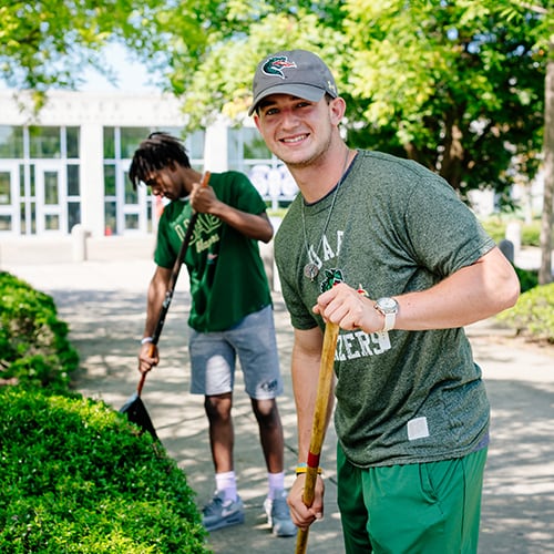 Two students raking leaves and smiling.