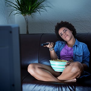 Student eating popcorn and pointing remote while watching TV.