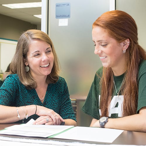 An advisor and student talking together at a table.