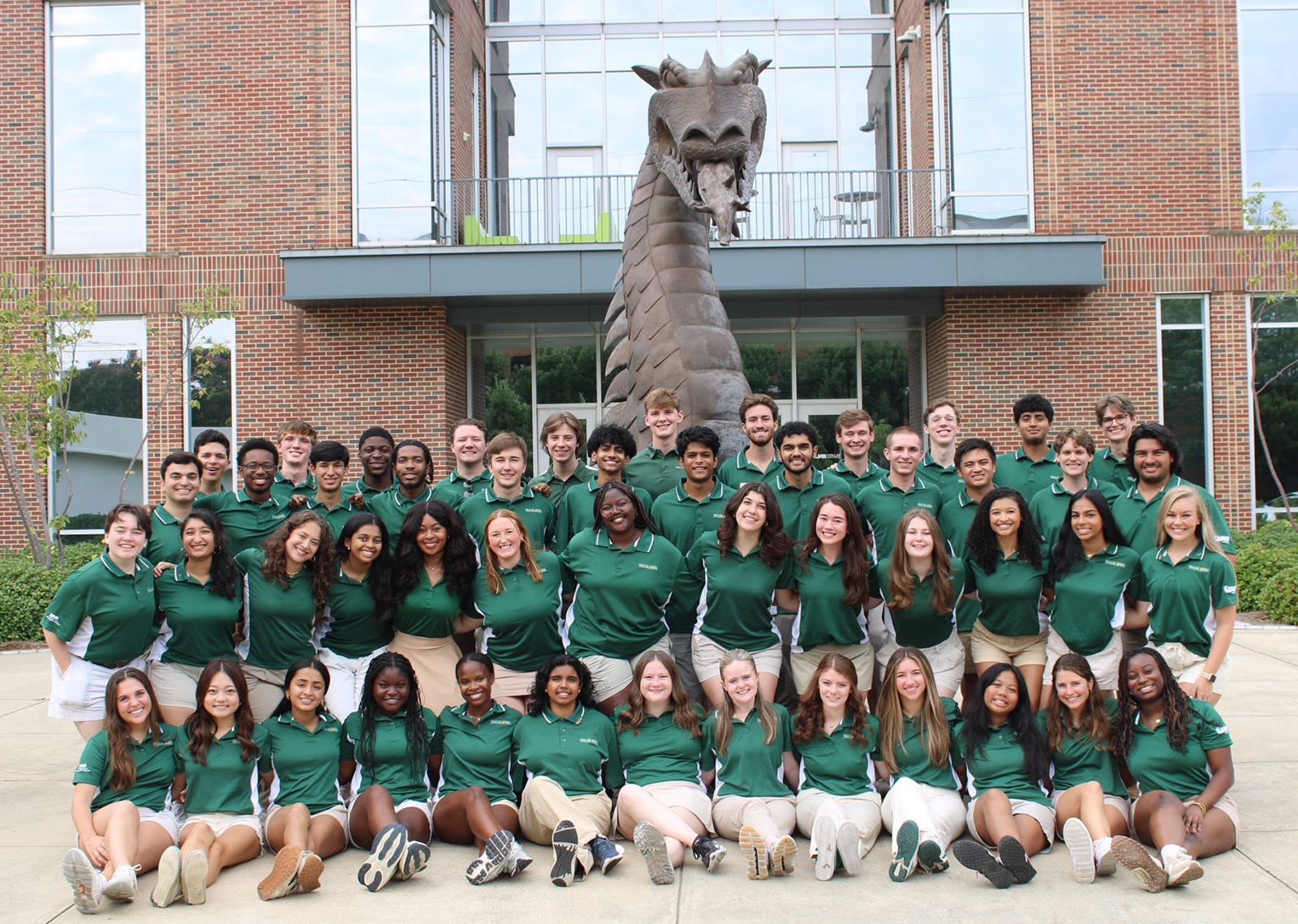 Smiling wearing their official green Trailblazers shirts posing around the bronze Blaze statue outside Collat School of Business.