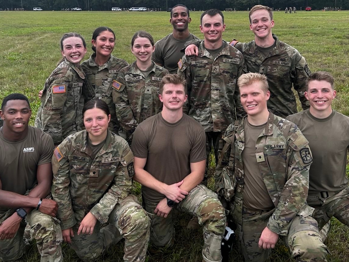 A group of trainees in camo pose on a grassy field.