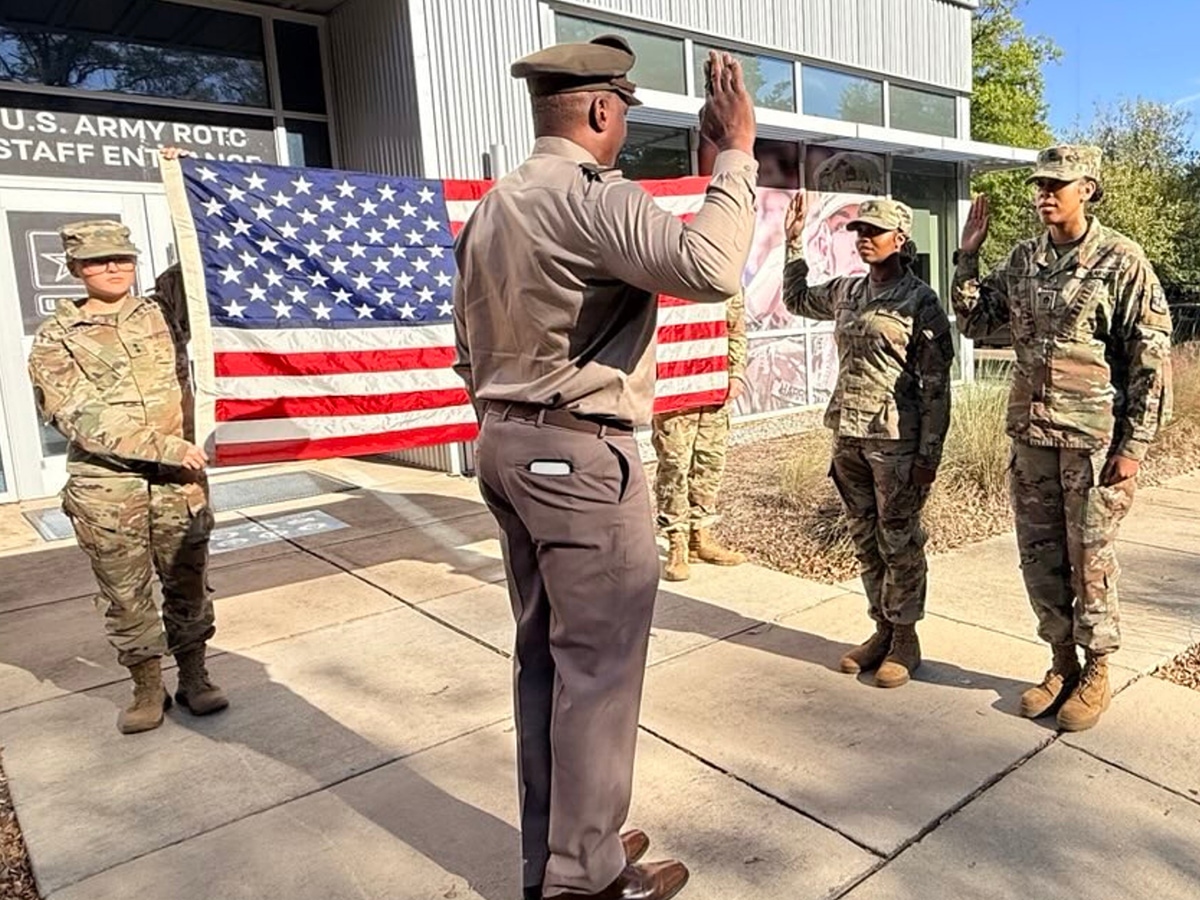 Trainees taking an oath in front of a commanding officer and two others holding a flag.