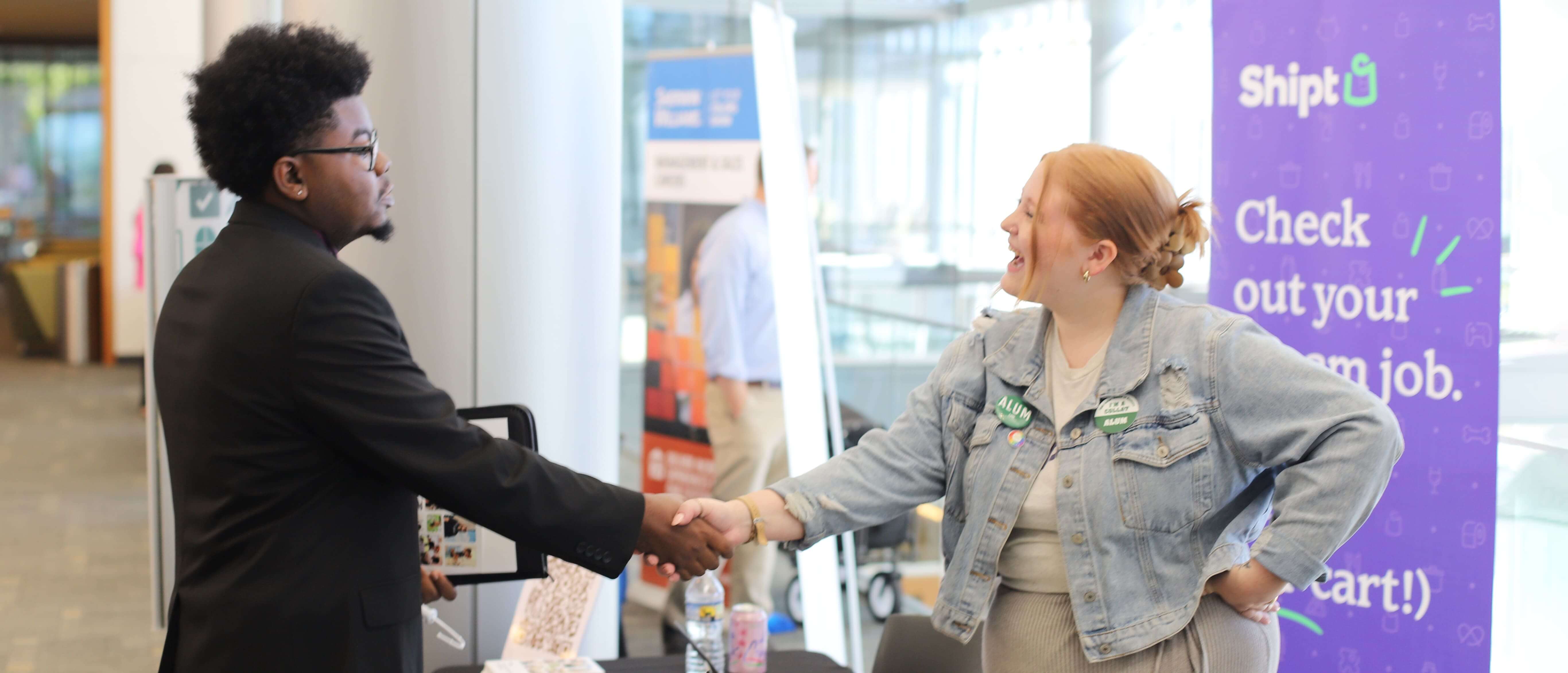 Black male student shaking hands with white female recruiter at career fair.