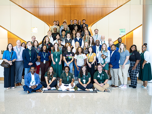 A large group of 50+ individuals smiling at the base of a staircase