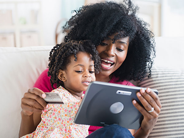 Smiling woman shopping on her tablet while her child watches.