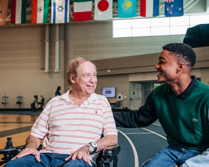 A man sitting and talking to another man in a wheelchair
