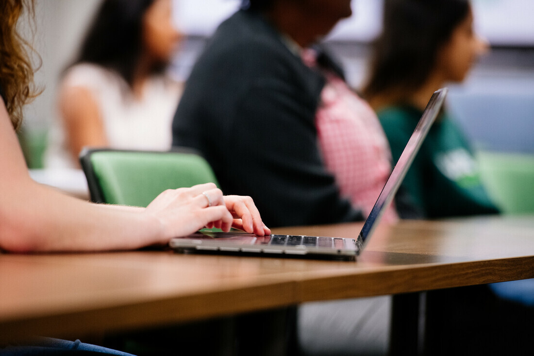 Simulation of a class taking place, focus is on a person using their laptop