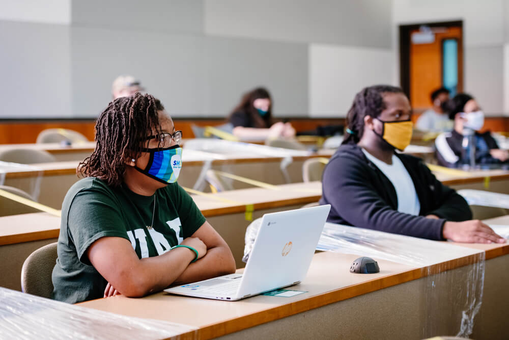 Students in facemasks in a classroom where seats have been marked off for social distancing. 
