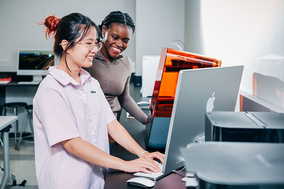 Two female students working with a 3-D printer. 