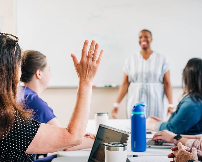 Students in a classroom, one with their hand raised.