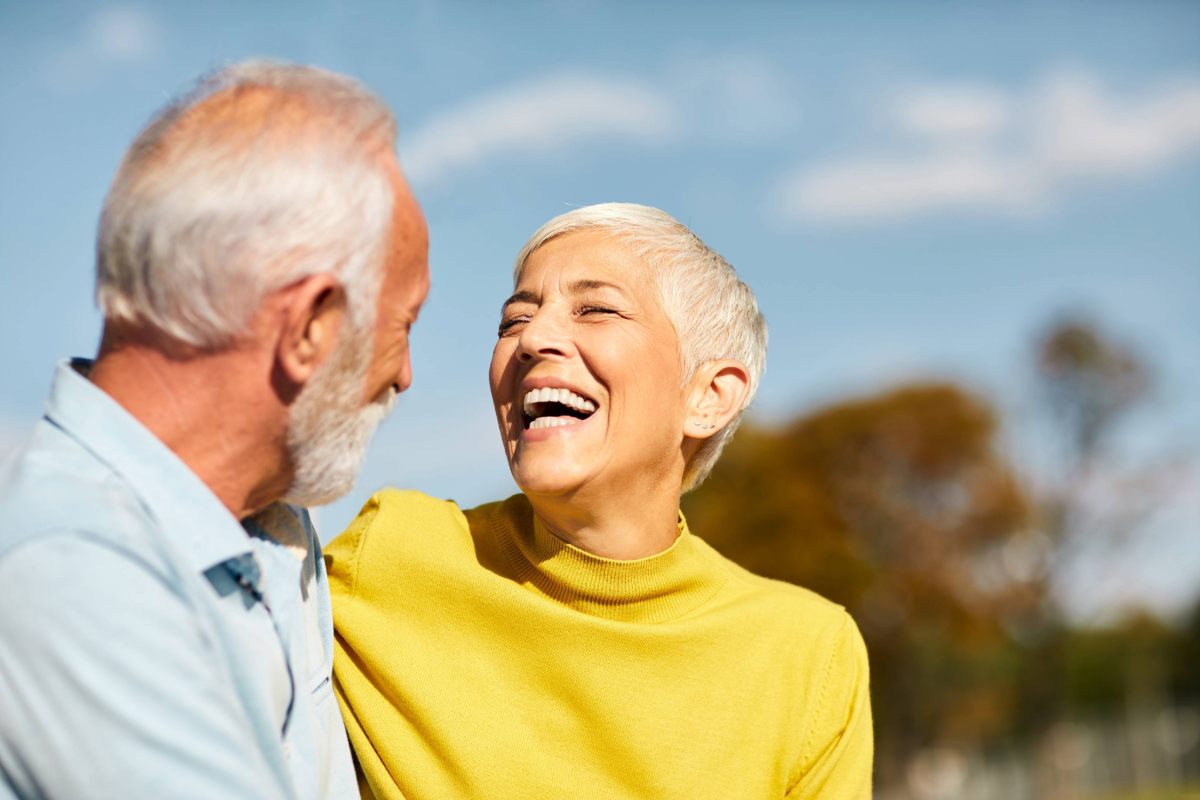 A senior couple smiling at each other in an outdoors setting