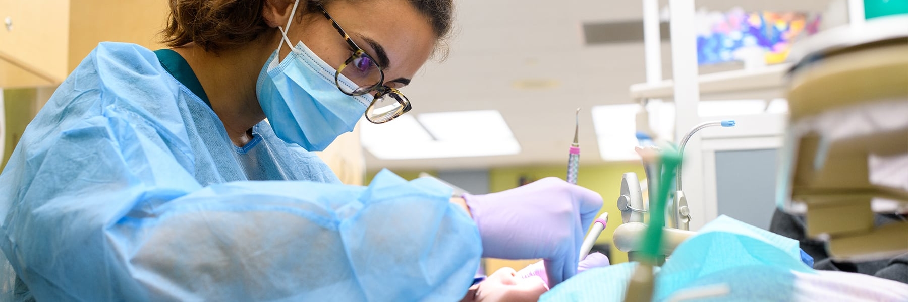 Dentist in mask and scrubs cleaning the mouth of a young boy.