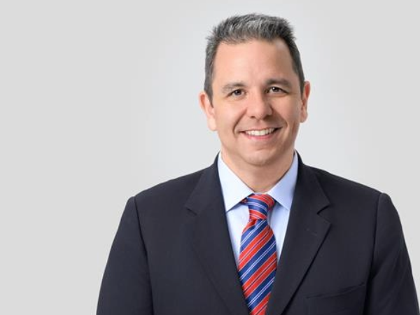 Man with grey hair and black suit smiling against a grey background