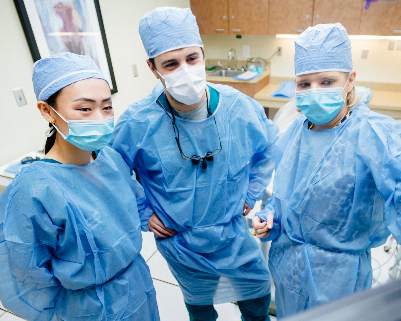 One dentist gesturing with her hands while talking to two other dentistd in front a screen with x-rays.