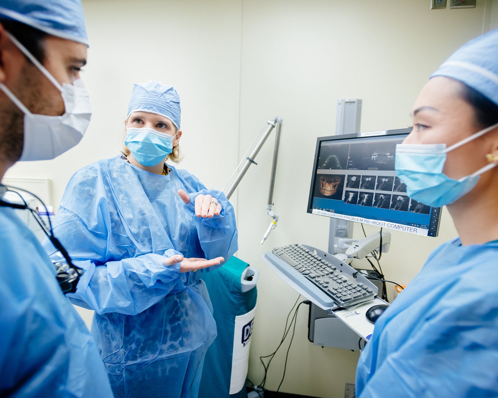 One dentist gesturing with her hands while talking to two other dentistd in front a screen with x-rays.