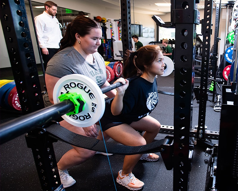 A female student spotting another weightlifting. 