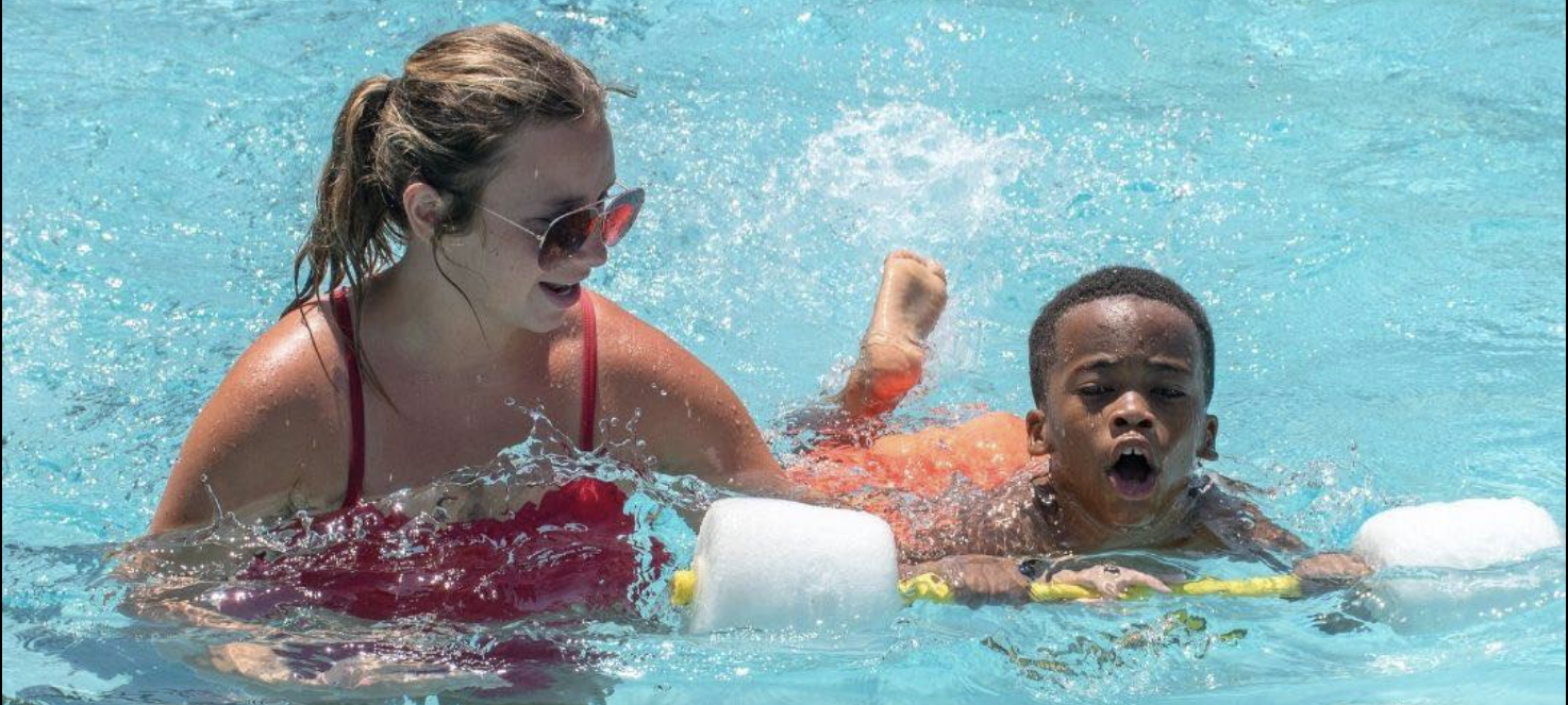 Photo of a female lifeguard helping a small boy swim in a YMCA pool