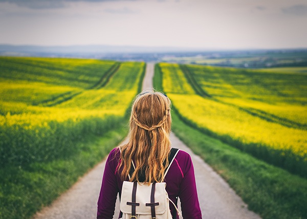 A woman with long red hair and a canvas backpack looks out over a winding path.