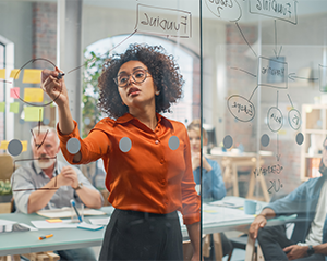 A standing woman writes on a transparent board covered in notes