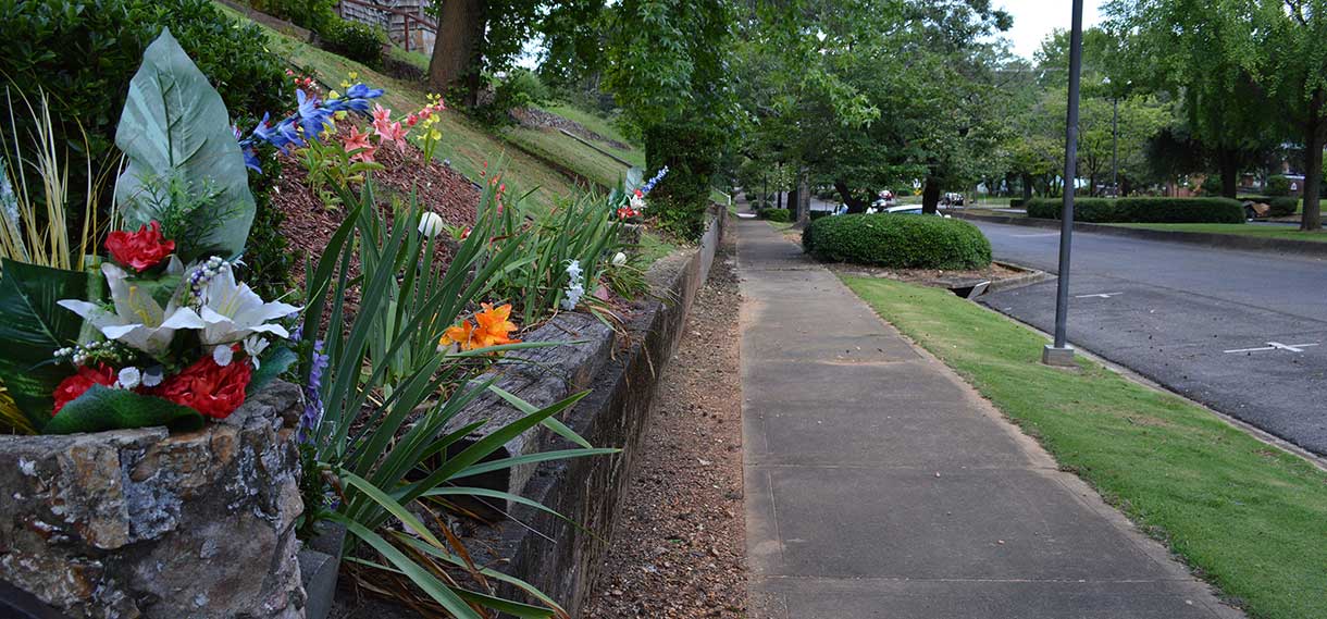 A wall next to a sidewalk with many flowers.