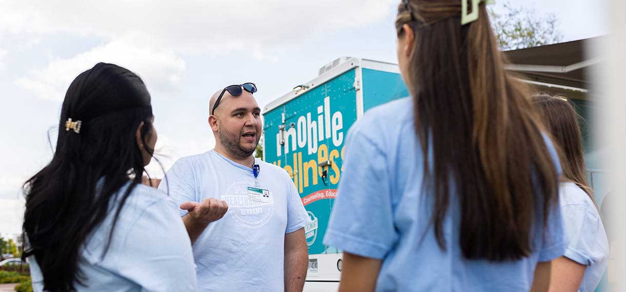 White male talking to people outside the mobile wellness van.