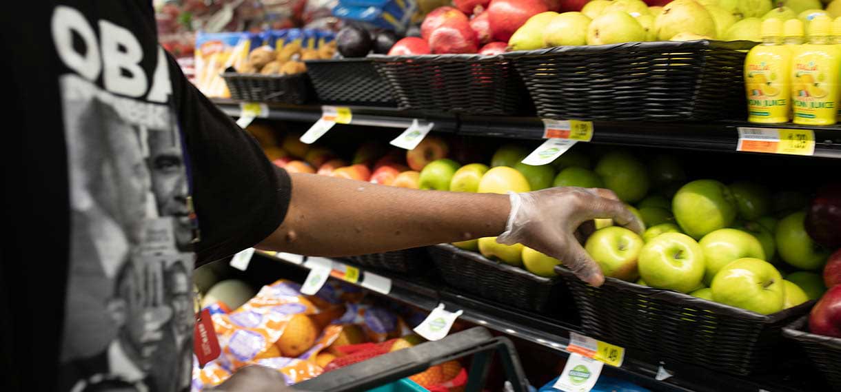 Someone in an Obama tshirt picks up a green apple from shelves of fruit.