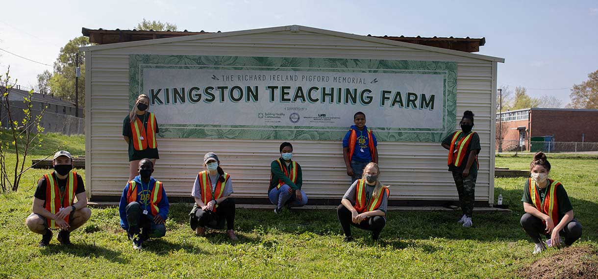 Volunteers outside of the Kingston Teaching Farm sign.