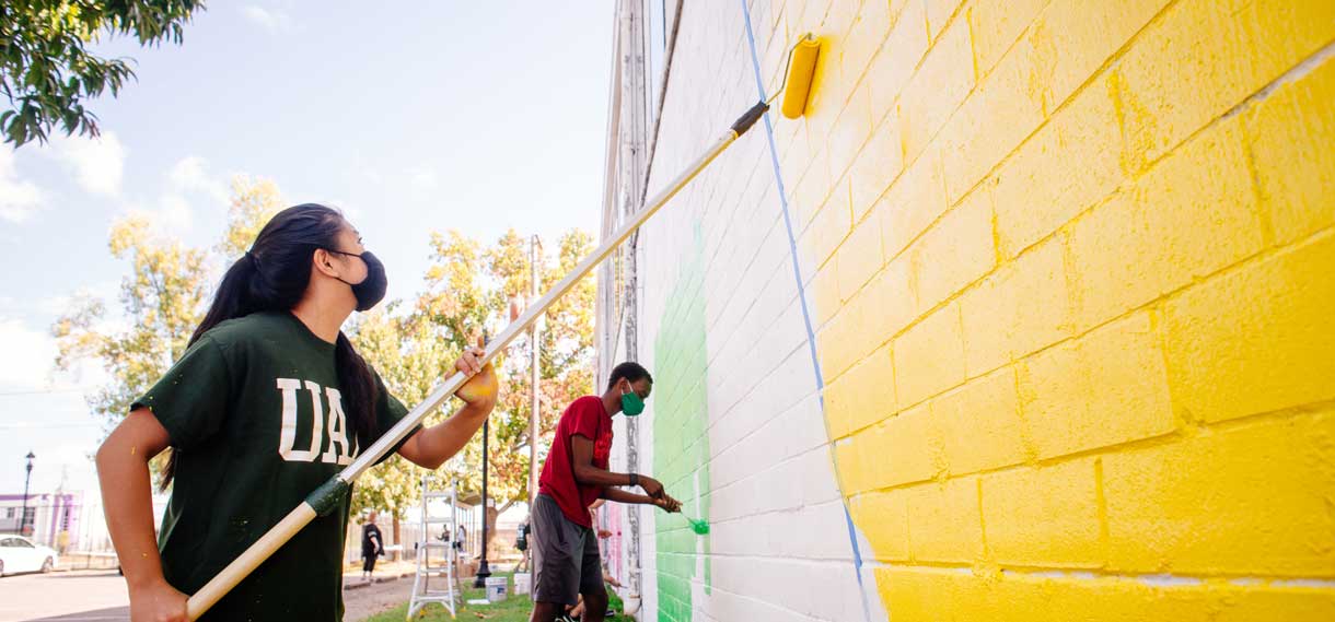 Mural painters use rollers to apply bright yellow and green paint.