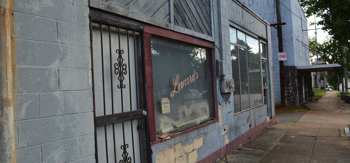 A cinderblock and glass storefront with "Leonard's" written in cursive on one window and decorate iron securite gate on the door.