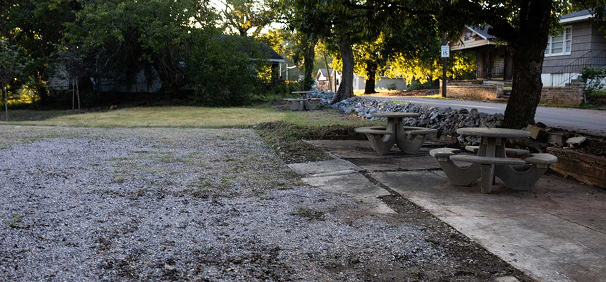Picnic area with two circular cement tables with benches in a cement and gravel area.