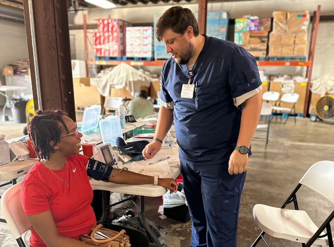 A bearded man takes an older Black woman's blood pressure.