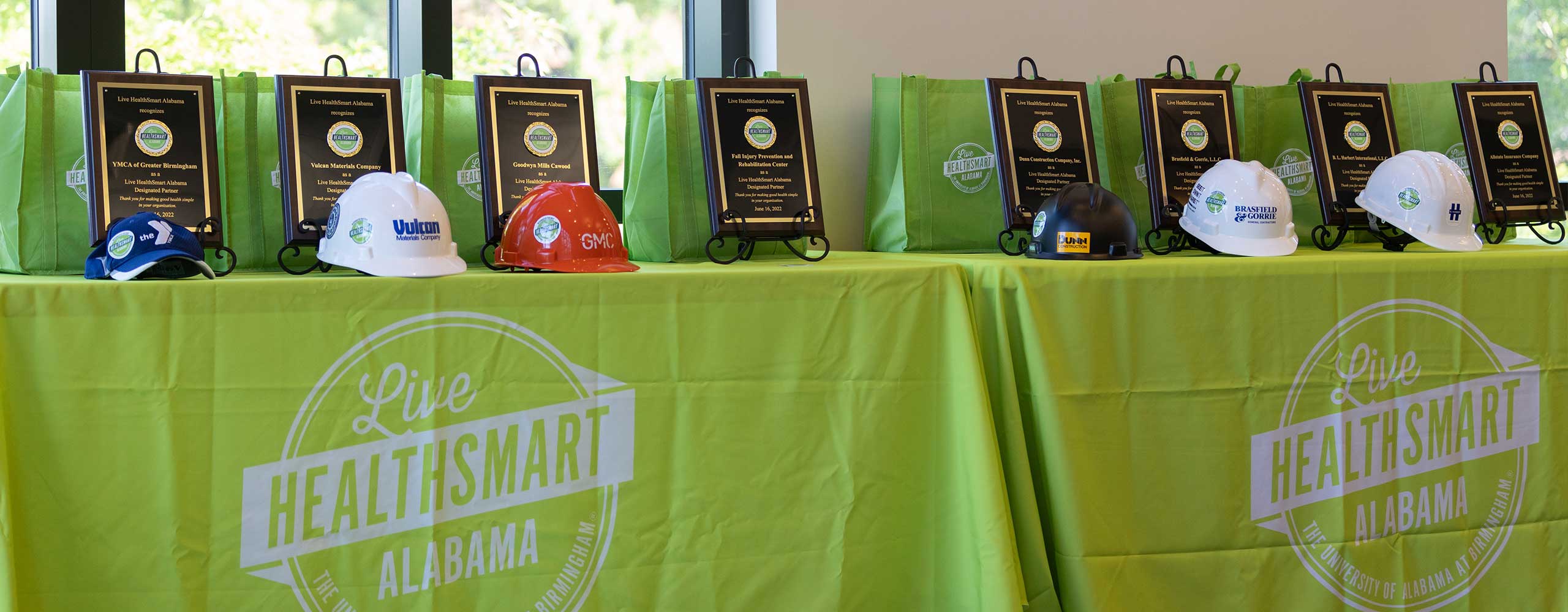A line of hard hats and plaques sit on tables covered in light green Live HealthSmart table clothes.