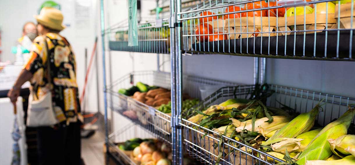 Shelves of veggies in the mobile market, patrons unfocused in the background.