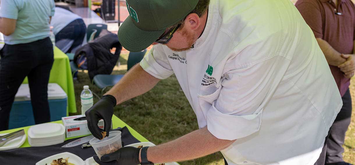 A man in gloves and a chef's jacket prepares food.