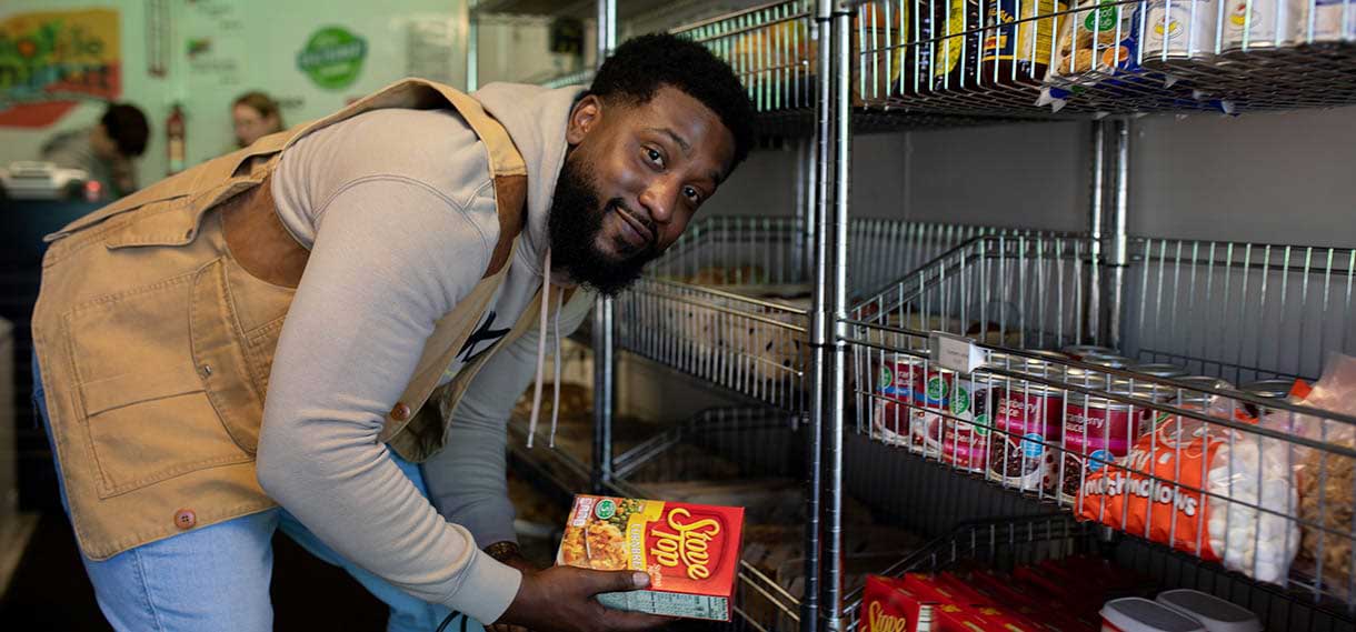 A bearded black male smiles at the camera as he gets a box of Stove Top from a shelf.