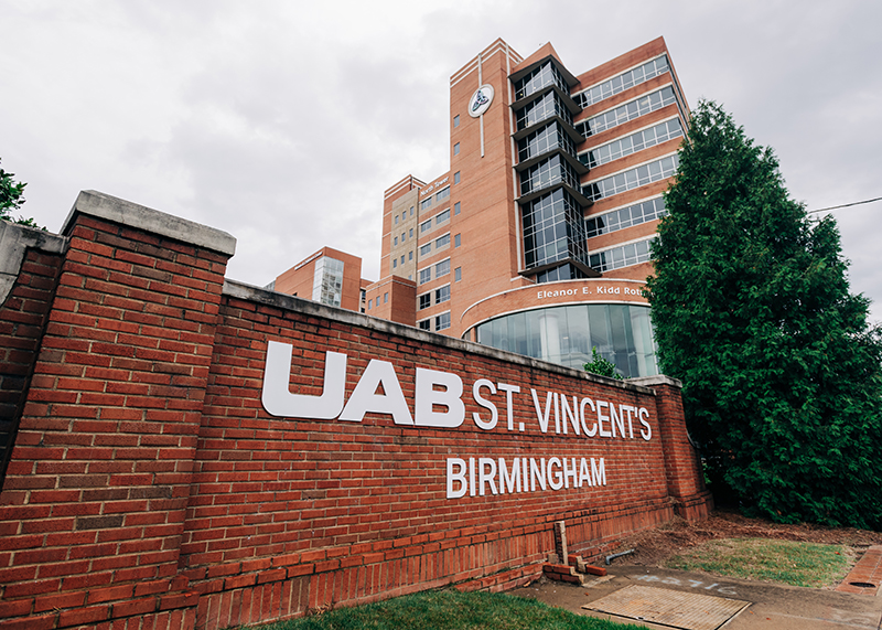 Close-up of brick roadside signage that reads "UAB St. Vincent's Birmingham" with large hospital building in background, November 1, 2024.