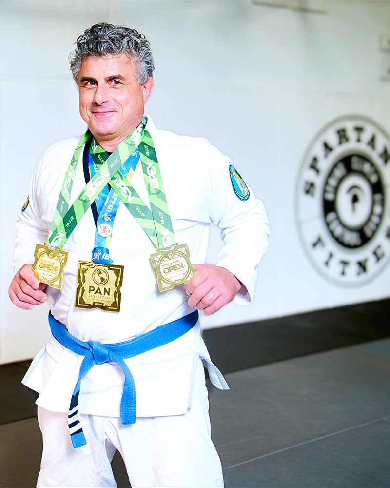 Distinguished professor Aurelio Galli, Ph.D., D.S.c, poses with three award medals from the Pan American juice-jitsu competition. Photo taken at Spartan Fitness training gym.