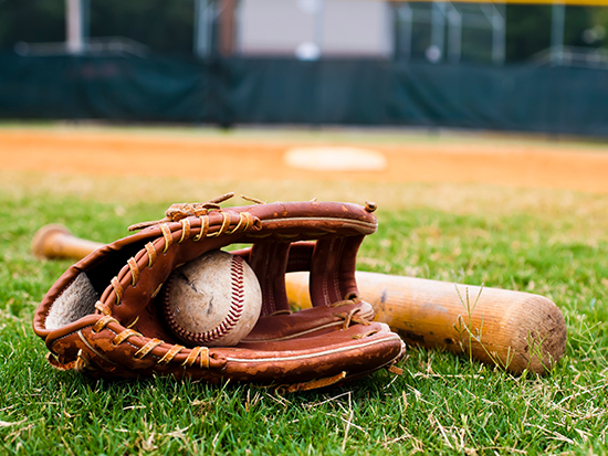 Old baseball, glove, and bat on field with base and outfield in background.