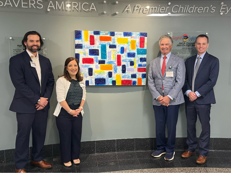 Four people stand beside a colorful abstract painting displayed in a hospital lobby