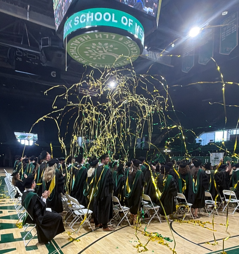 Medical students celebrate together as green and gold streamers fall around them at the end of Commencement 2026.