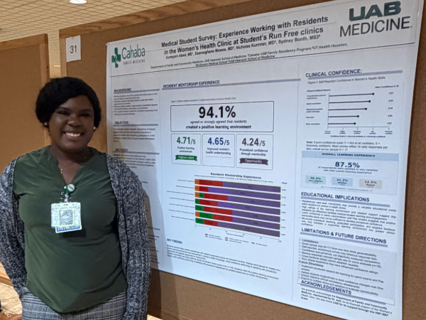 Poster presenter poses in front of poster.