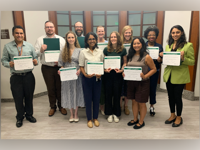 Group of faculty and staff holding certificates of completion and posing for a photo in a hallway.