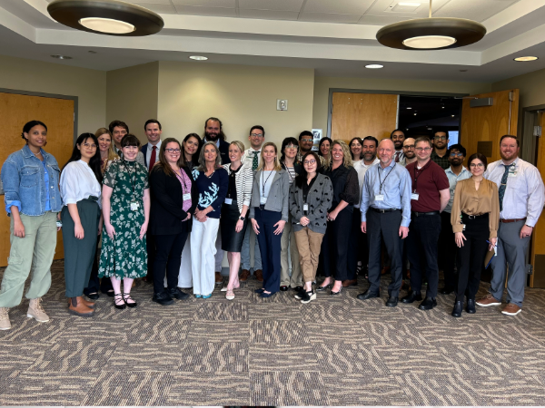 Group photo of participants and faculty posing in front of doors to a conference room