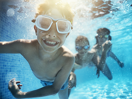 Happy kids having underwater party in the swimming pool. The boy is grinning at the camera. Shot with Nikon D850.