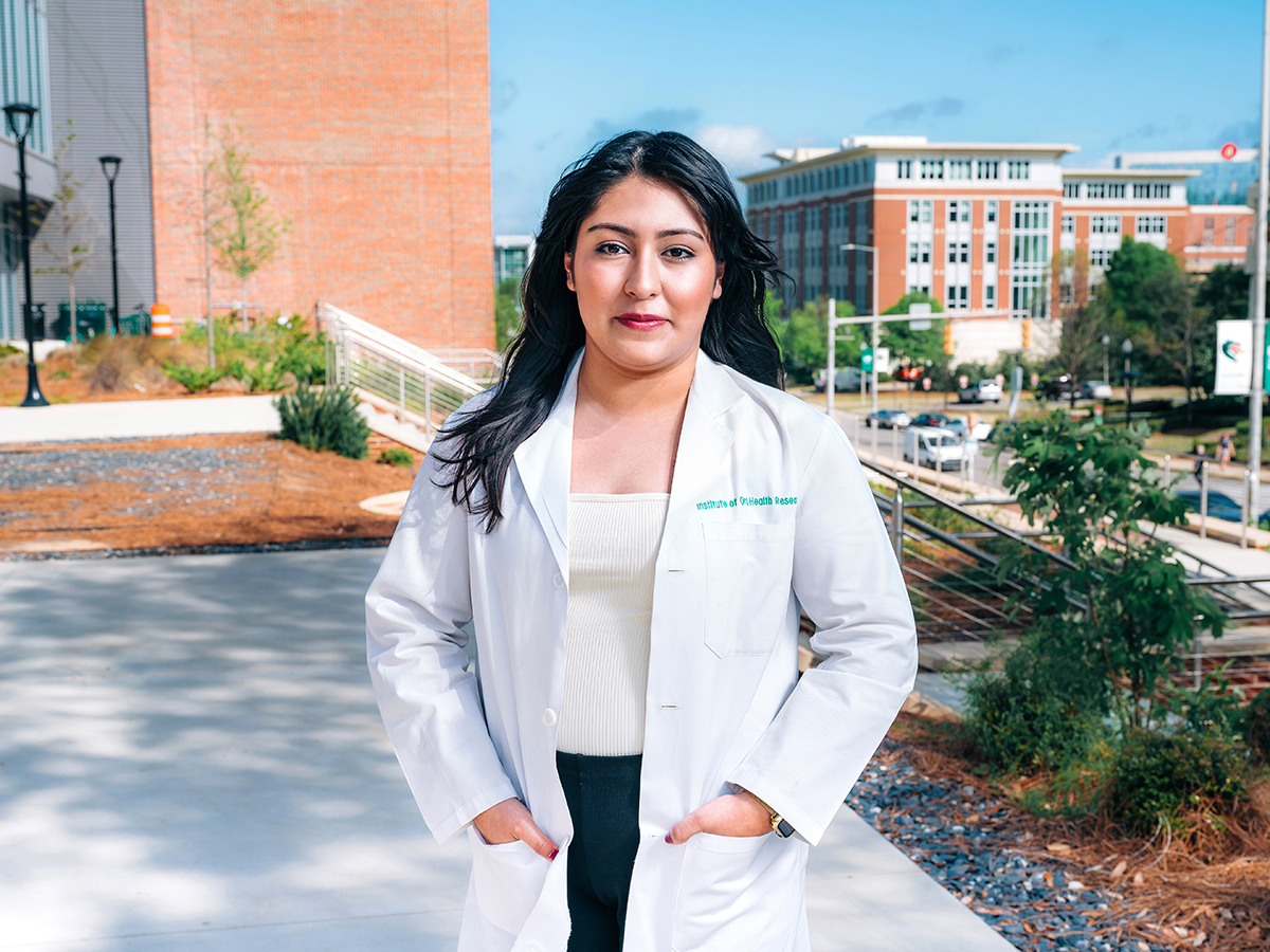Jacqueline Hernandez-Burgos in her lab coat in front of buildings on UAB's campus.