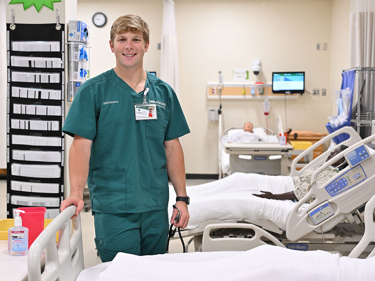 Tyler Waugh in the nursing simulator lab in his UAB green nursing scrubs.