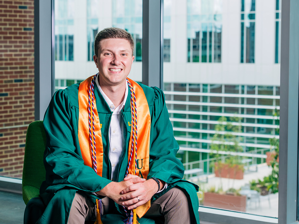 Headshot of Jon Kinney in his green UAB graduation gown with a gold stole. 
