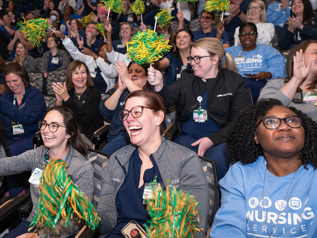 UAB Hospital Receives Magnet Nursing Designation for Record 6th Time by the American Nurses Credentialing Center Magnet Recognition Program. Overall of smiling nursing students and staff celebrating by cheering and shaking UAB green and gold shakers (pom poms) at the announcement event in Margaret Spain Auditorium, April 2024.