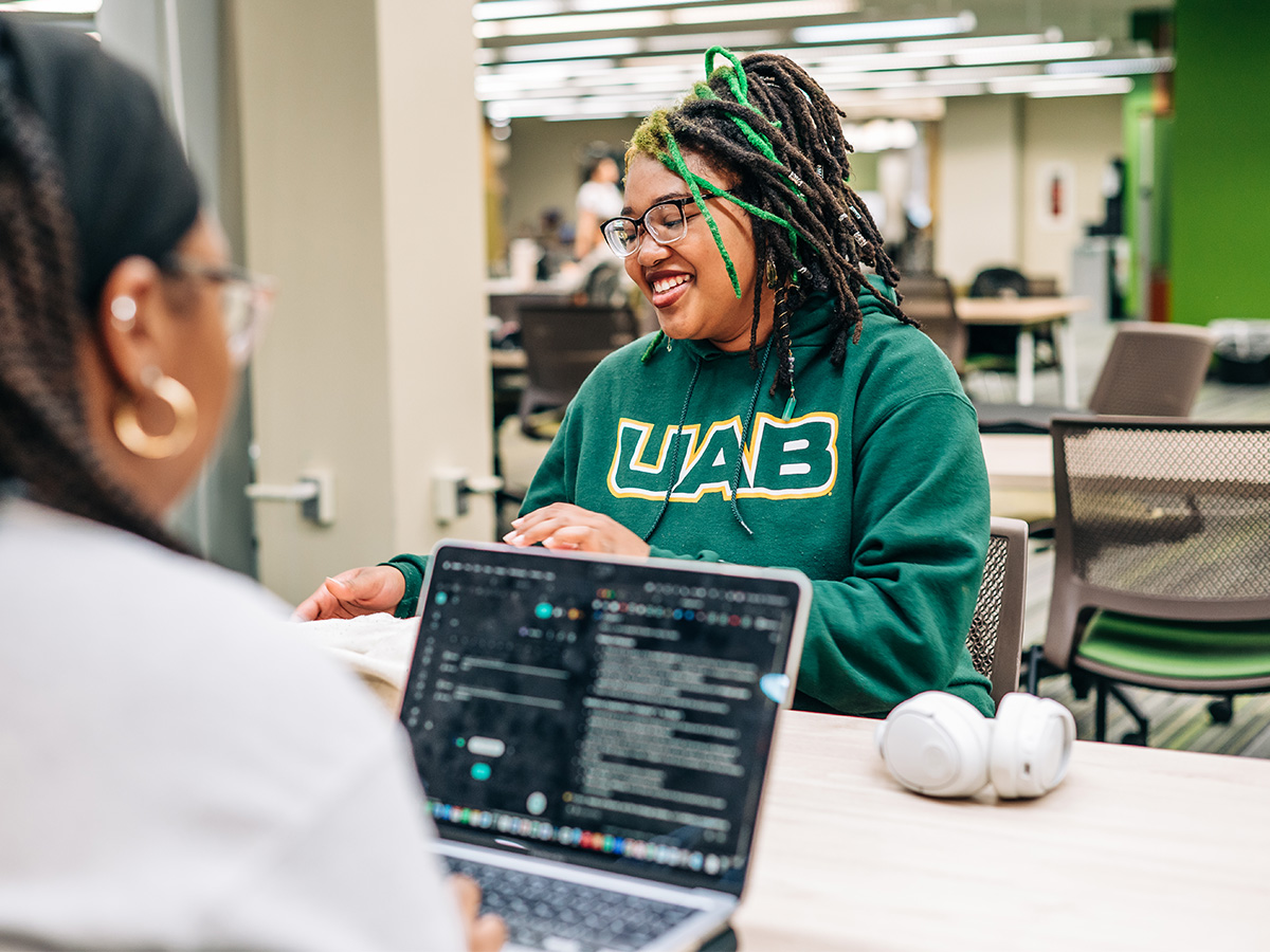 A student in a green UAB shirt smiles while studying. 