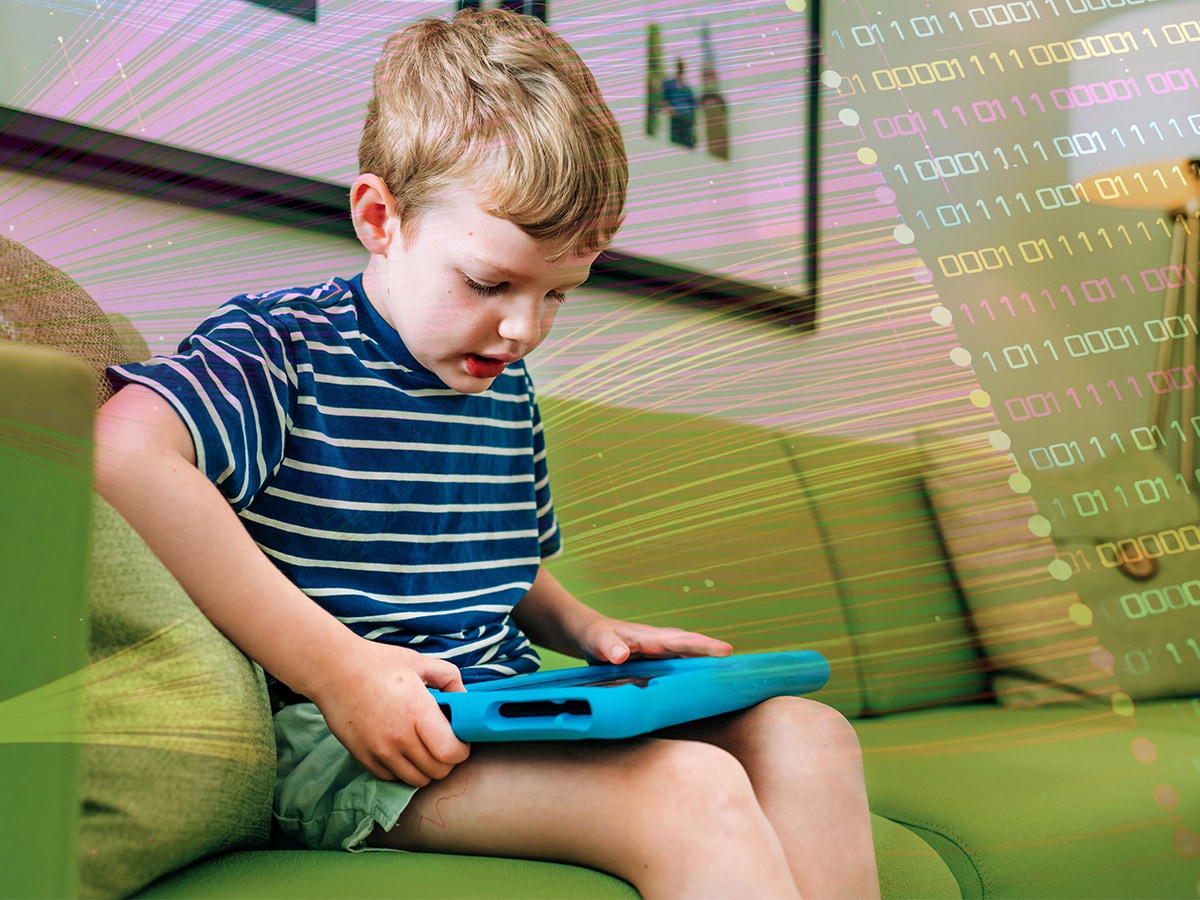  Elementary-aged child is sitting on sofa while working/playing on tablet computer at home